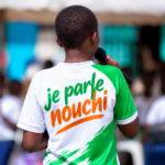 Jeune intervenant vu de dos prenant la parole devant un public, avec l’inscription « je parle nouchi » sur son tee-shirt